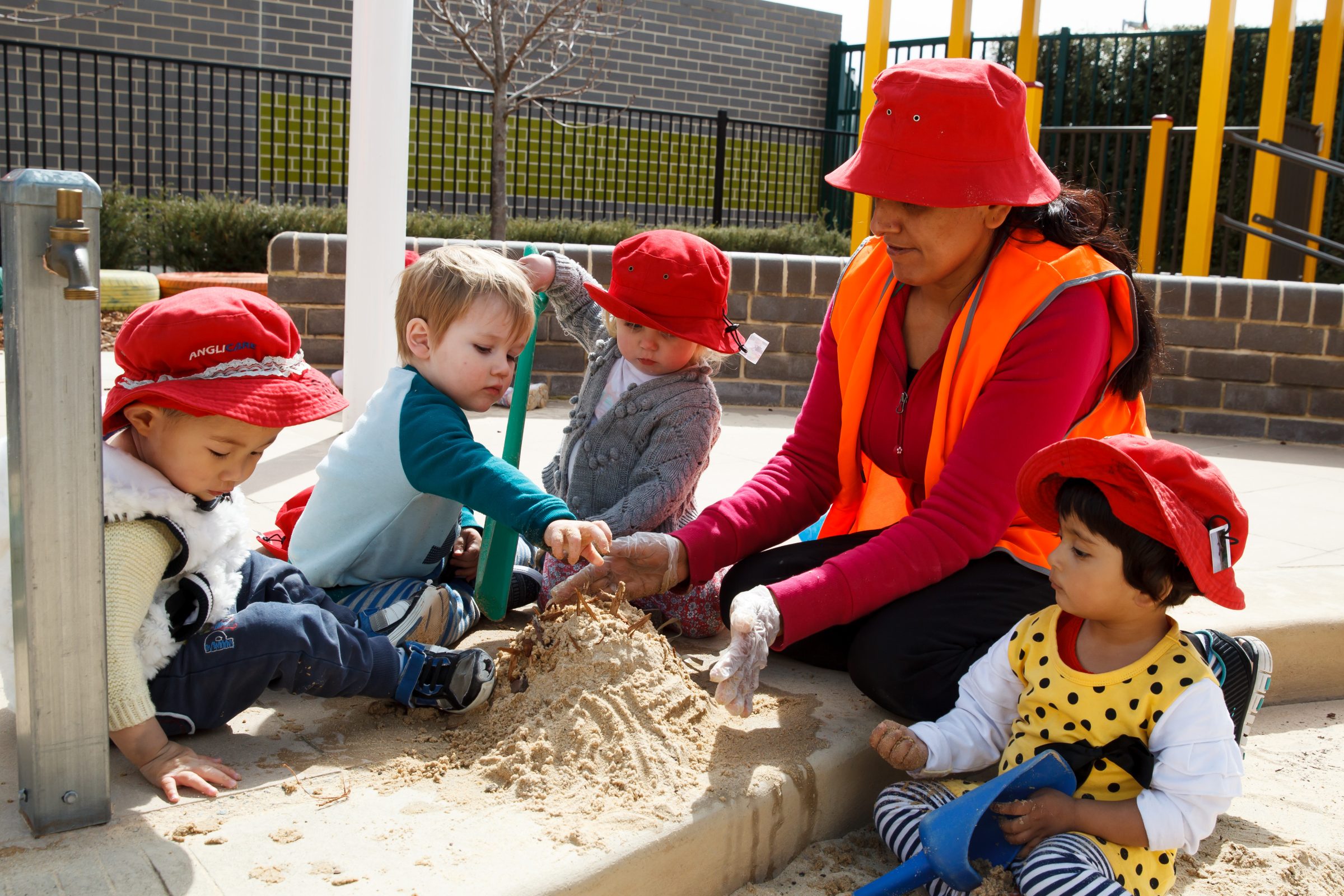 educator playing in sandpit with 4 toddlers