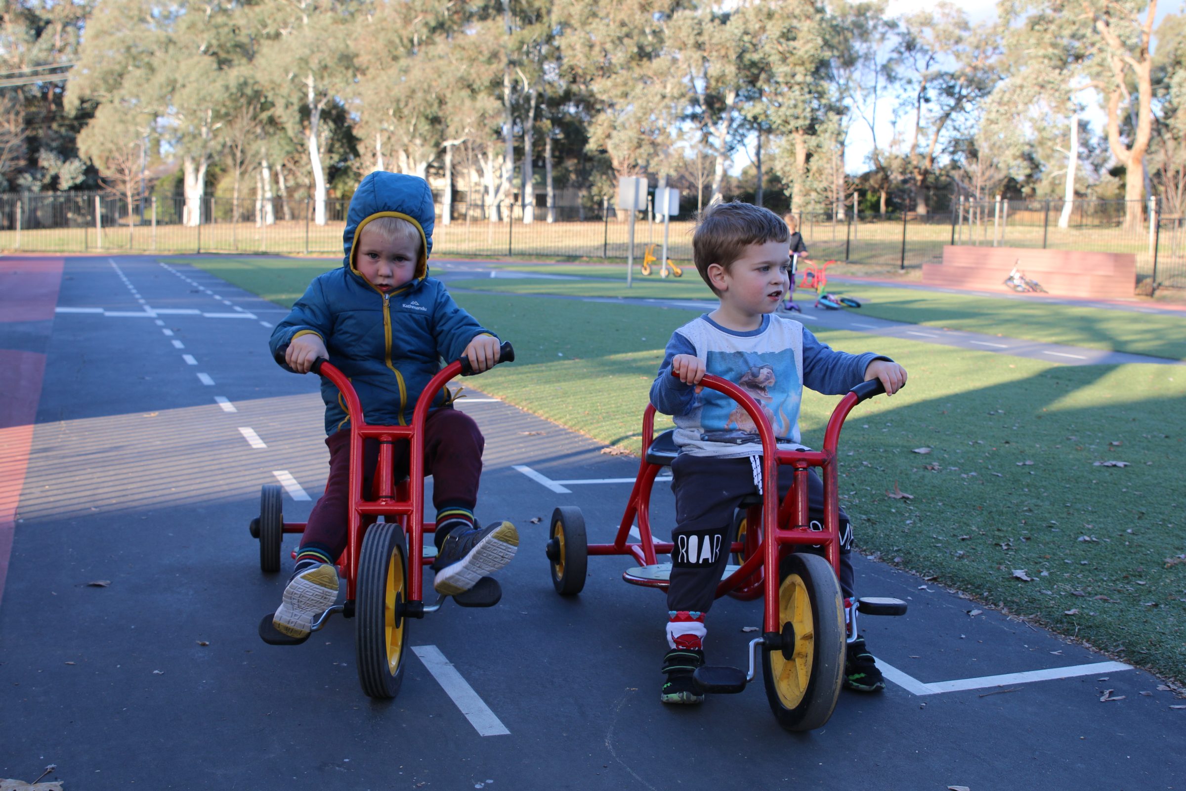 two preschoolers riding red tricycles