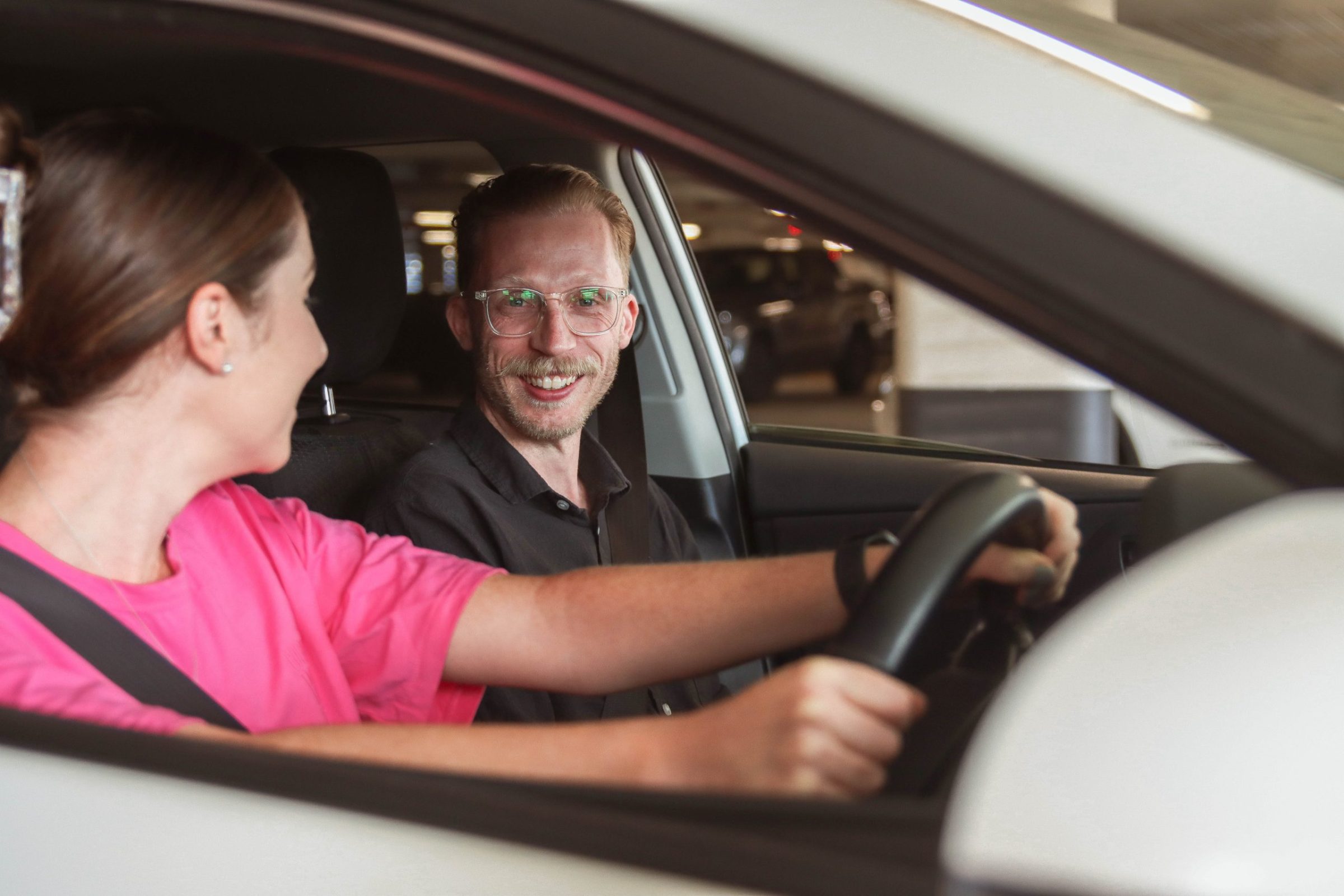 Two people sitting in car, Anglicare team member sitting in the passenger seat smiling at the camera.