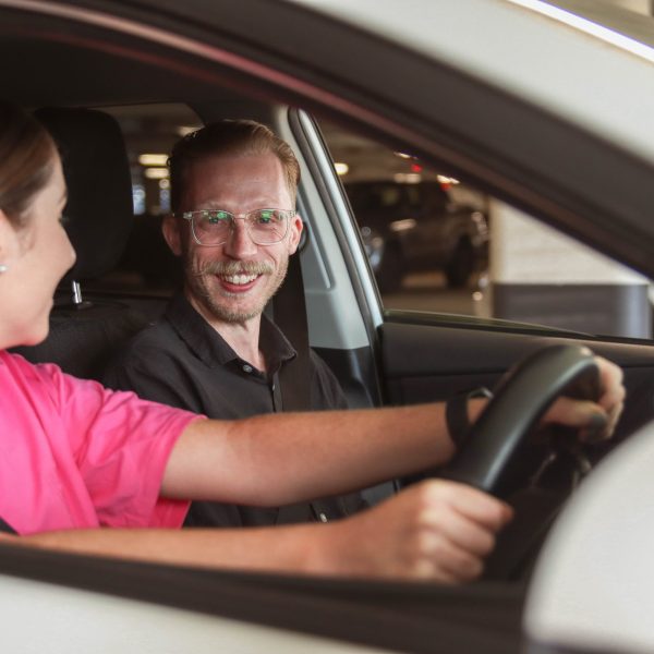 Two people sitting in car, Anglicare team member sitting in the passenger seat smiling at the camera.